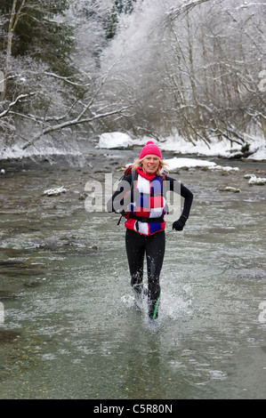 Ein Läufer ignoriert das kalte Wasser und genießt einen verschneiten Flussüberquerung Bett. Stockfoto
