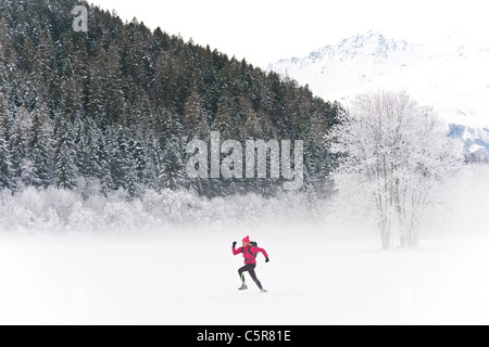 Ein Jogger läuft durch eine verschneite Berglandschaft. Stockfoto
