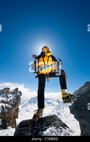 Weibliche Bergsteiger steht hoch über den Gipfeln mit Sauerstoffmaske, Eispickel und Steigeisen. Stockfoto