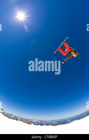 Ein Snowboarder springt hoch in einem sonnigen blauen Himmel. Stockfoto