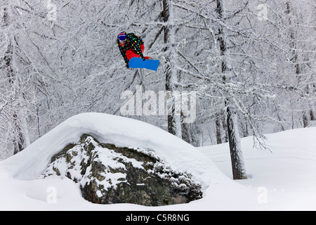 Ein Snowboarder startet einen Sprung in einem verschneiten Wald. Stockfoto