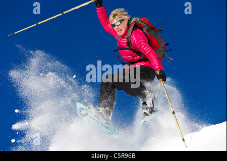 Eine Frau Schneeschuhwandern springt durch frischen Pulverschnee. Stockfoto