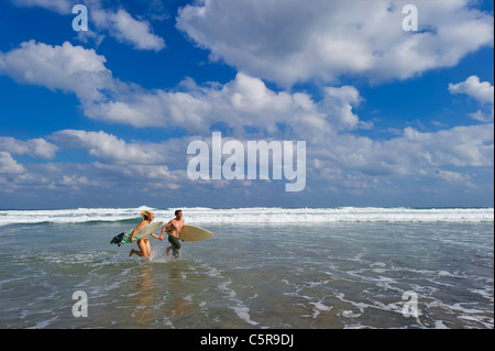 Zwei Surfer laufen hand in hand durch die Wellen. Stockfoto