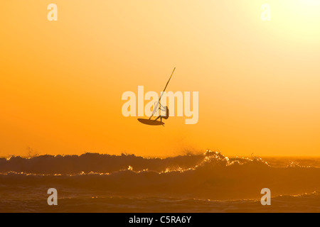 Ein Windsurfer springt eine Ozeanwelle in einem Sonnenuntergang. Stockfoto