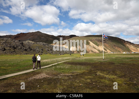 Die isländische Flagge mit Menschen, die zu Fuß in Richtung der heißen Quellen von Landmannalaugar im Bereich Fjallabak Islands Stockfoto