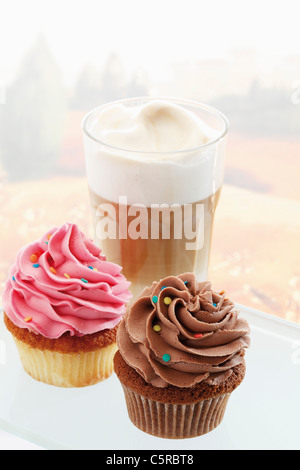 Nahaufnahme von Buttercreme Cupcakes mit Glas Latte macchiato Stockfoto