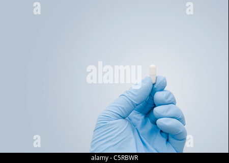 Coronavirus Covid-19 Impfstoff-Heilungskonzept. Hand in Blau Gummihandschuh Aus Chirurgischem Gummi, mit einem einzigen weißen Kapselkübel Stockfoto