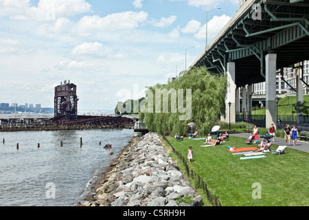 Familien & Freunde Sonnen am Rasen am Ufer neben dem erhöhten Autobahn während Spaziergänger & Fahrräder in Riverside Park New York pass Stockfoto