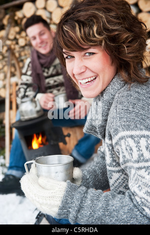 Österreich, Salzburger Land, Flachau, junger Mann und Frau, die Zubereitung von Tee und sitzen neben Ofen im winter Stockfoto