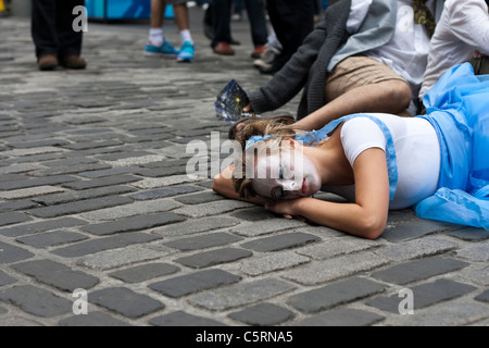 Eine weibliche Darstellerin liegt auf dem Kopfsteinpflaster von Edinburghs Royal Mile Förderung ihrer Show im Rahmen des Fringe festival Stockfoto