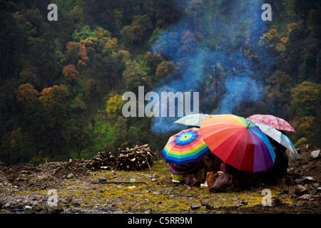 Straßenarbeiter Zuflucht unter ihren Sonnenschirmen wie es nieselt. Tawang, Arunachal Pradesh. Indien Stockfoto