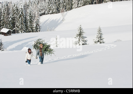 Österreich, Salzburger Land, Flachau, junger Mann und Frau mit Weihnachtsbaum im Schnee Stockfoto