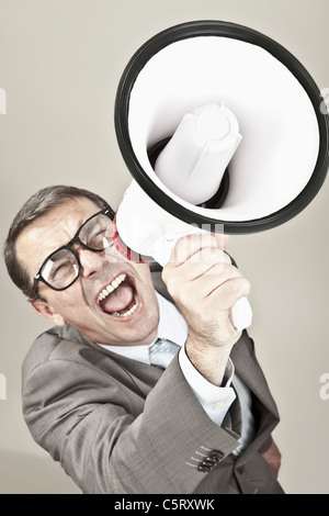 Nahaufnahme von Geschäftsmann schreien über Megaphon vor grauem Hintergrund Stockfoto