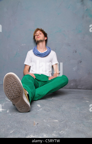 Junger Mann sitzen und schiefen Agaist schmutzigen Wand, portrait Stockfoto
