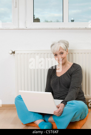 Deutschland, Düsseldorf, Frau mit Laptop in der Nähe von Heizung zu Hause, Lächeln, Porträt Stockfoto