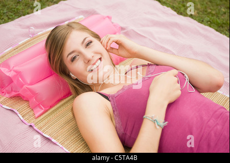 Deutschland, Bayern, Starnberger See, junge Frau liegend auf Decke, MP3-Player anhören, Lächeln, erhöhte Ansicht, Porträt Stockfoto