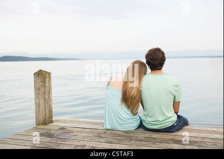 Deutschland, Bayern, Starnberger See, junges Paar sitzt am Steg, Rückansicht Stockfoto