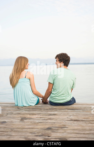 Deutschland, Bayern, Starnberger See, junges Paar sitzt am Steg, Rückansicht Stockfoto