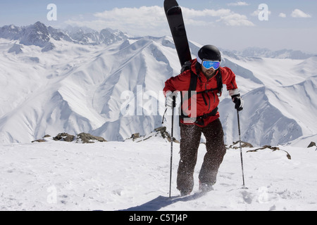 Indien, Kaschmir, Gulmarg, Mann mit Skiern am Rücken bergauf gehen Stockfoto