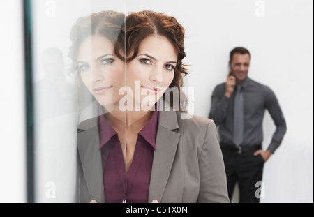 Deutschland, Köln, Geschäftsfrau, stehen nächste Glastür, Mann im Hintergrund mit Handy Stockfoto