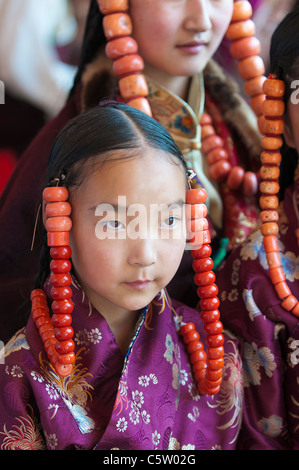 Junge Mädchen tragen von schweren Korallen Schmuck warten bei Schamanen Erntefest, Tongren, Qinghai Provinz, China Stockfoto