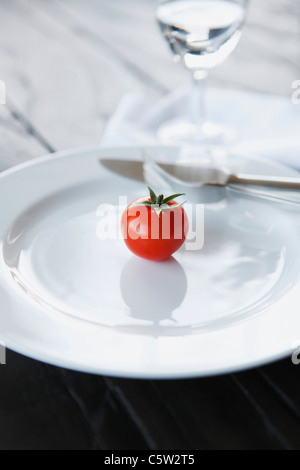 Einzelne Tomate und Besteck auf weißen Teller, Nahaufnahme Stockfoto