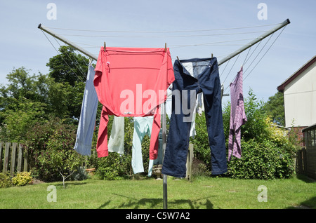 Nasse Haushaltskleidung, die an einer Drehwaschleitung hängend ist, um an einem warmen sonnigen Tag im Freien in einem heimischen Garten zu trocknen. Großbritannien. Stockfoto