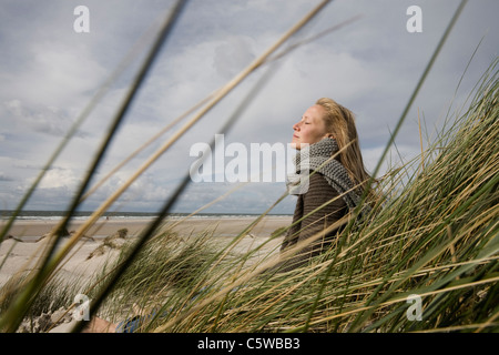 Deutschland, Schleswig-Holstein, Amrum, junge Frau auf grasbewachsenen Sanddüne, Augen geschlossen Stockfoto