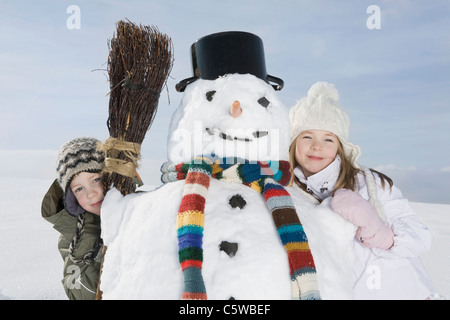 Deutschland, Bayern, München, (8-9) jungen und Mädchen (8-9) stehen neben Schneemann, Porträt Stockfoto