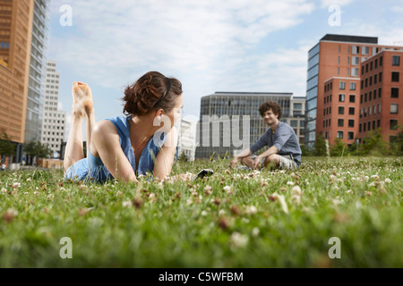 Deutschland, Berlin, junge Frau liegend in Wiese halten Handy-Mann im Hintergrund Stockfoto
