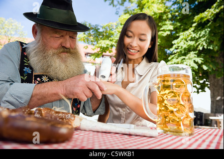 Deutschland, Bayern, Oberbayern, Bayerischer Mann und Asiatin in Bier Garten, asiatische Frau testen ein Ort von Schnupftabak Stockfoto