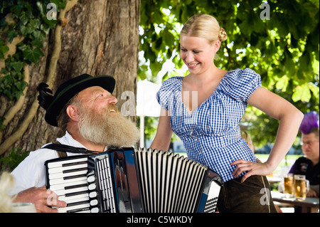 Deutschland, Bayern, Oberbayern, Senior Mann in traditioneller Tracht spielt Akkordeon im Biergarten Stockfoto