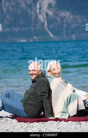 Deutschland, Bayern, älteres Paar am Seeufer entspannen, sitzen Rücken an Rücken Stockfoto