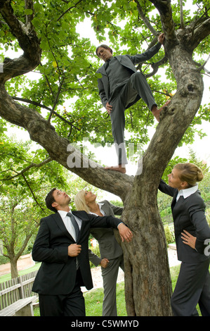 Deutschland, Geschäftsleute stehen unter Baum, ein Mann, der auf Zweigen Stockfoto