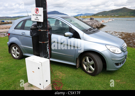 Auto geparkt auf dem Rasen neben "Parkverbot auf Rasen-Zeichen". Valentia Island, County Kerry, Irland Stockfoto