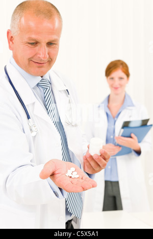 Arzt Team Senioren männlich halten junge Kollegin Pillen Stockfoto