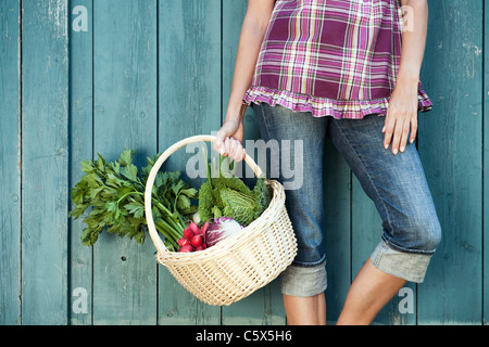 Deutschland, Bayern, Frau lehnte sich gegen Scheunentor hält Korb mit frischem Gemüse Stockfoto