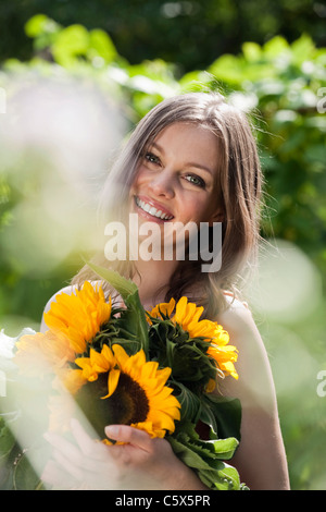 Deutschland, Bayern, Frau Holding Bündel von Sonnenblumen, Lächeln, Porträt Stockfoto