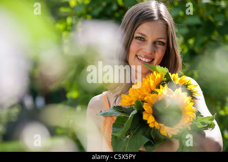 Deutschland, Bayern, Frau Holding Bündel von Sonnenblumen, Lächeln, Porträt Stockfoto