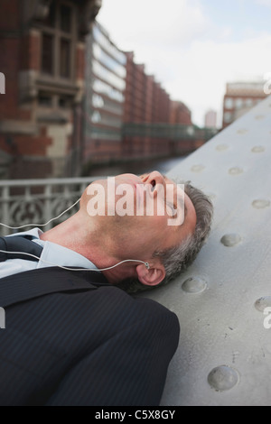 Deutschland, Hamburg, Geschäftsmann auf Rücken liegend, mit MP3-player Stockfoto