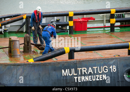 Arbeiter auf einem Schlepper Schiff bereiten eine Aufbocken Lastkahn, der Offshore-Windpark Walney, Barrow in Furness, Cumbria, UK zu schleppen. Stockfoto