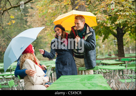 Deutschland, Bayern, englischer Garten, Biergarten, vier Personen im regnerischen Bier Garten sprechen Stockfoto