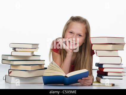 Mädchen mit Buch neben Stapel Bücher vor weißem Hintergrund, Lächeln, Porträt Stockfoto