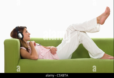 Junge Frau auf Sofa mit Kopfhörern, Seitenansicht Stockfoto