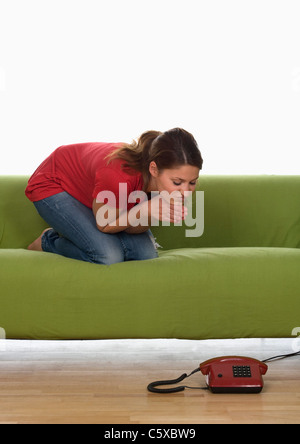 Junge Frau sitzt auf dem Sofa, beobachten das Telefon Stockfoto