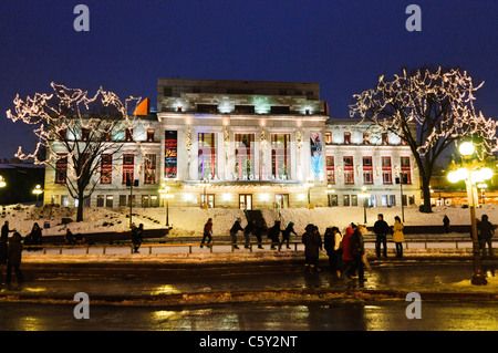 QUEBEC CITY, Kanada – Eisläufer gleiten über eine Eisbahn vor dem eleganten Palais Montcalm. Die beleuchtete Fassade des historischen Gebäudes bietet eine atemberaubende Kulisse für Wintererholung im Herzen des Kulturviertels von Quebec City. Stockfoto