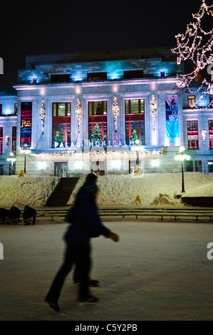 QUEBEC CITY, Kanada – Eisläufer gleiten über eine Eisbahn vor dem eleganten Palais Montcalm. Die beleuchtete Fassade des historischen Gebäudes bietet eine atemberaubende Kulisse für Wintererholung im Herzen des Kulturviertels von Quebec City. Stockfoto