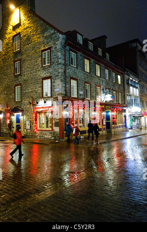 QUEBEC CITY, Kanada – Eine malerische Kopfsteinpflasterstraße in der Altstadt von Quebec glitzert nach leichtem Regen unter dem warmen Licht der Straßenlaternen. Der nasse Glanz auf der historischen Straße spiegelt die charmante Architektur und die sanfte Beleuchtung wider und schafft eine romantische Atmosphäre in diesem UNESCO-Weltkulturerbe. Stockfoto