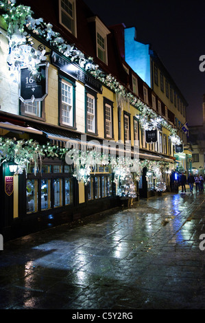 QUEBEC CITY, Kanada – Eine malerische Kopfsteinpflasterstraße in der Altstadt von Quebec glitzert nach leichtem Regen unter dem warmen Licht der Straßenlaternen. Der nasse Glanz auf der historischen Straße spiegelt die charmante Architektur und die sanfte Beleuchtung wider und schafft eine romantische Atmosphäre in diesem UNESCO-Weltkulturerbe. Stockfoto