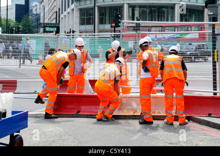 Gut sichtbare Kleidung Schutzhelm und Teamwork viele Hände arbeiten zusammen sieben Arbeiter bauen Stahlzaunplatten an Straßenbauarbeiten in Victoria London England Großbritannien an Stockfoto